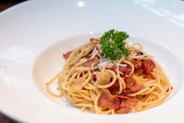 Spaghetti with bacon in white plate for eating concept. Spicy spaghetti with bacon and basil. Spaghetti with pork sausage and tomato sauce on white plate.