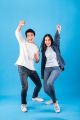 Excited young Asian couple man and woman happy celebrate success over blue background, winner...
