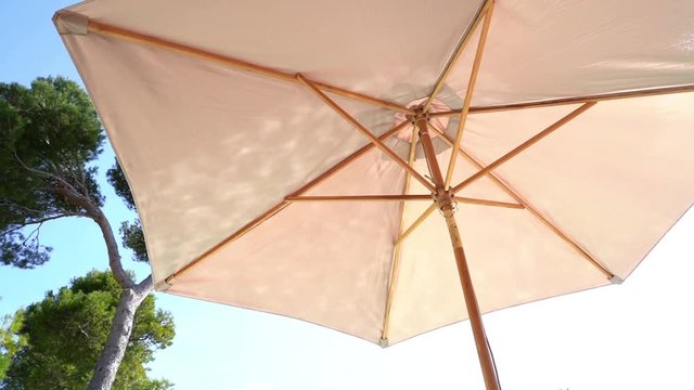 parasol beige avec reflets de la piscine et pins dans le fond sur un ciel bleu