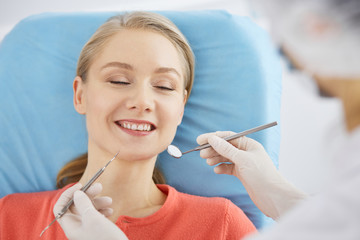 Smiling caucasian woman is being examined by dentist at dental clinic. Healthy teeth and medicine, stomatology concept