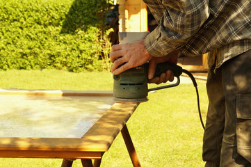 preparation grinding woodwork outside. Close-up details of Male hand sanding a door with a random orbital sander in spring. Concept of renovation works, Carpentry details with woodwork and handyman. 