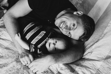Young dad and baby are lying in bed and smiling. Black and white photo of a young dad and baby.