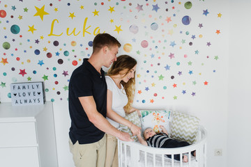 Young parents look at their baby in the crib.