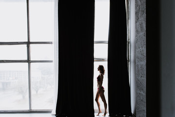 Silhouette of a young woman in underwear near the window.