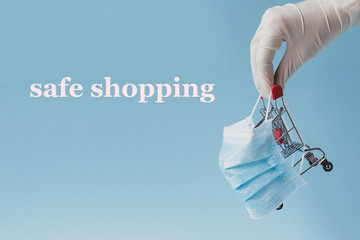 Safe shopping concept . Covid-19 sars time. Hand in medicine glove holds a shopping cart in mask ....