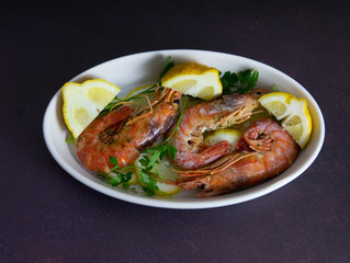 roasted prawns with lemon slices in white baking dish 