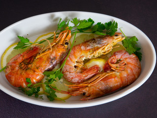 roasted prawns with lemon slices in white baking dish 