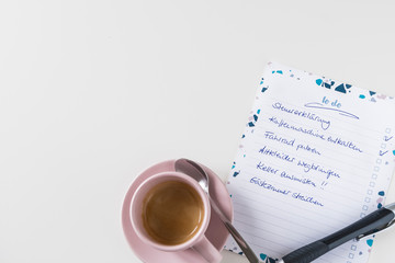 Handwritten german to-do list, pen and coffee on white table.