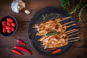 Plate with grilled chicken skewers and herbs on dark wood.