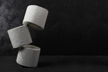 Toilet paper rolls stack besides dark concrete background. White toilet paper with copy space.