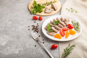 Boiled pork tongue with tomatoes and herbs on a gray concrete background. Side view, copy space.