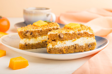 Homemade cake with persimmon and pumpkin and a cup of coffee on a white wooden background with orange textile. side view, selective focus.