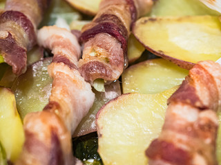 Raw spring onion with rolled bacon. Typical Sicilian street dish called 'Cipollata' roasted on the grill and roasted potatoes as a side dish.