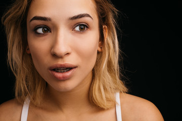 Amazed wonder young woman look right. Blonde girl posing on camera. Isolated over black background.