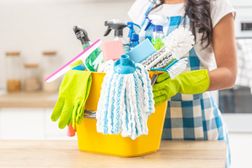 Bucket full of house clenaing stuff on a kitchen desk with a female holding it in rubber gloves