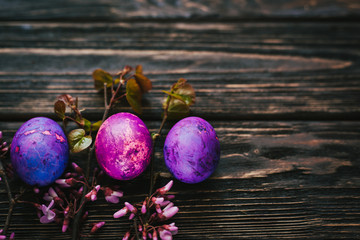 three purple easter eggs on dark wooden background