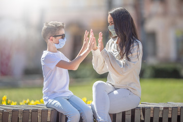 Boy and young woman giving a high five with both hands sitting in exterior, weraing face masks