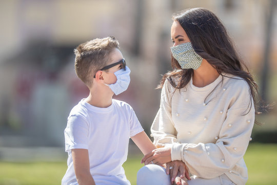 Mother And Son Wearing Face Masks Look At Each Other Sitting Outside