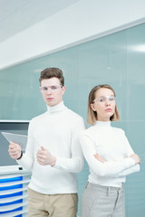Two young serious modern technologies center consultants in white jumpers