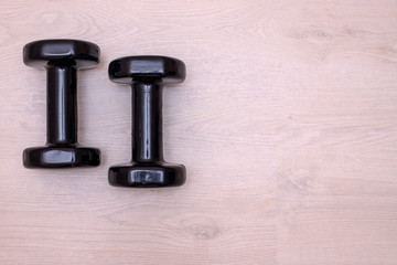 two small black dumbbells lie on the light floor of the room