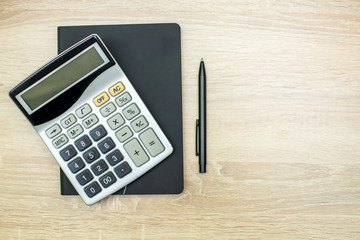a black diary, a black ballpoint pen, and a silver calculator with black and gray buttons lie on a...