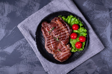 Grilled beef steak served on the stone plate with lettuce leaf and cherry tomatoes