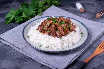 Stewed chicken gizzards on the boiled rice. Hot meal with offal meat products