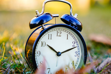 Image of spring Time Change. Summer back concept. Vintage alarm Clock outdoors. alarm clock on green grass 