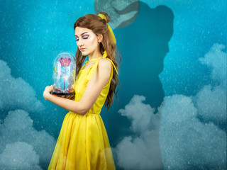 Woman in the yellow dress with red rose in her hands on the background of the beast . Beauty and...