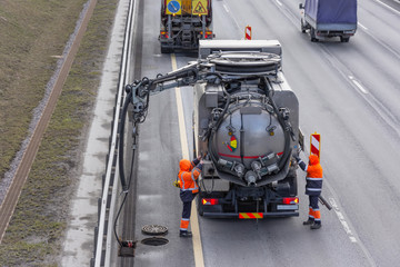 Sludge washer truck suction machine and workers specialists at work on the side of the highway to...