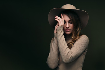 A young attractive blonde woman in a beige sweater, fedora hat and brown leather trousers poses on...