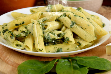 penne in a sauce with spinach and cheese in a white bowl on a wooden kitchen board