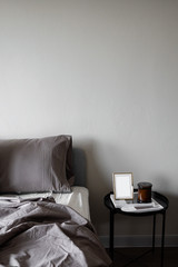 Bedroom corner grey velvet bed with soft pillows setting decorated with circular metal night table and beige painted wall in the background / cozy interior design