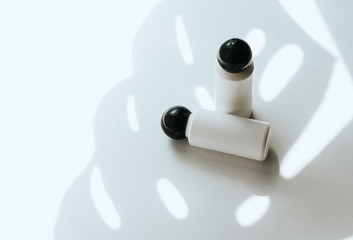 Two white empty plastic bottles on a white background with a shadow of a tropical leaf. Shampoo, shower gel or balsam concept