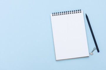 White clean notepad on black spring with black pencil on pastel blue paper background with copy space, top view. White spiral notepad on blue backdrop