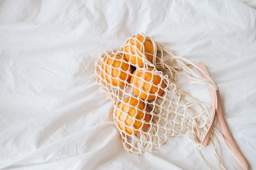 Fototapeta na wymiar Mesh eco bag with fresh oranges on a white cloth at home. Top view