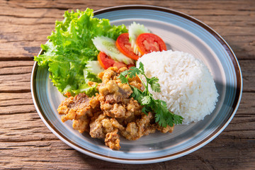 Fried pork topped with rice, served with lettuce, cucumber, tomato, arrange a beautiful dish, put on a wooden table.