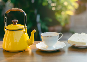 Yellow teapot on the wood table and white tea cup,Nature daylight and green garden,Afternoon rest time to relax from working at house,Home stay campaign to reduce the outbreak of the covid virus 2019.