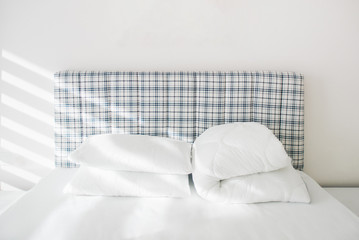 Two white and new pillows and a blanket on a comfortable bed with a white sheet in a modern white interior. Homeliness. Hotel room. Bedding.