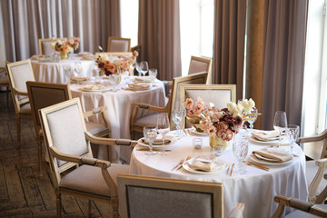 Luxury cozy autumn wedding table decoration in the restaurant. Fresh and dried flowers, roses, carnations. Beautiful table setting: golden appliances, fork and knife, calligraphy guest seating card.