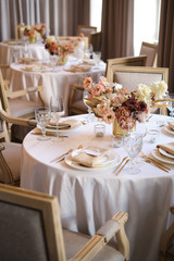 Luxury cozy autumn wedding table decoration in the restaurant. Fresh and dried flowers, roses, carnations. Beautiful table setting: golden appliances, fork and knife, calligraphy guest seating card.