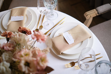 Luxury cozy autumn wedding table decoration in the restaurant. Fresh and dried flowers, roses, carnations. Beautiful table setting: golden appliances, fork and knife, calligraphy guest seating card.