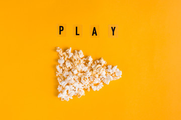 Popcorn in the shape of play button and text PLAY on yellow background. Flat lay banner, top view....