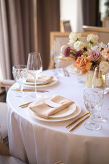 Luxury cozy autumn wedding table decoration in the restaurant. Fresh and dried flowers, roses, carnations. Beautiful table setting: golden appliances, fork and knife, calligraphy guest seating card.