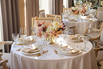Luxury cozy autumn wedding table decoration in the restaurant. Fresh and dried flowers, roses, carnations. Beautiful table setting: golden appliances, fork and knife, calligraphy guest seating card.