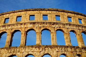 Obraz premium Amazing facade of stone Roman amphitheater through whose window place you can see blue sky