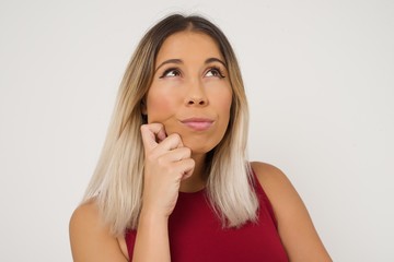 Portrait of thoughtful  woman keeps hand under chin, looks away trying to remember something or listens something with interest, dressed casually, poses indoors. Youth concept.