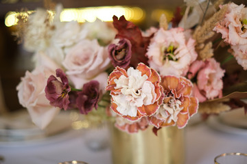 Luxury cozy autumn wedding table decoration in the restaurant. Fresh and dried flowers, roses, carnations. Beautiful table setting: golden appliances, fork and knife, calligraphy guest seating card.