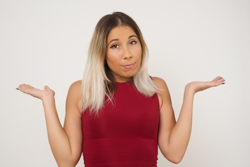 Fototapeta premium Puzzled and clueless young woman with arms out, shrugging her shoulders, saying: who cares, so what, I don't know. Negative human emotions, facial expressions, life perception and attitude.