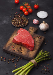Slice of Raw Beef sirlion steak on wooden chopping board with tomatoes,garlic and asparagus tips.